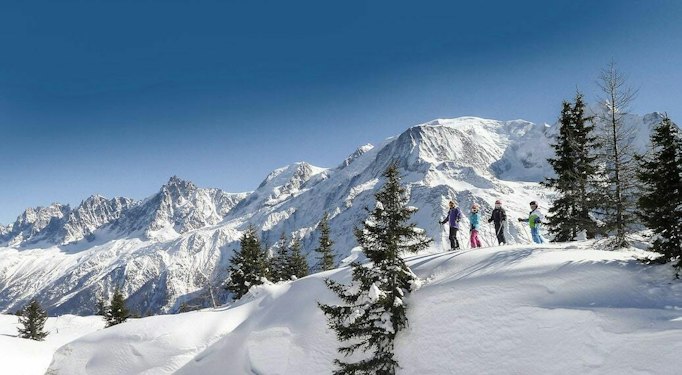 Skieurs sur une crête boisée des Houches face aux sommets enneigés