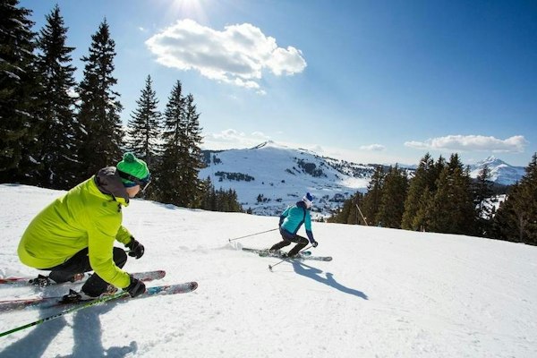 Deux skieurs en virage sur une piste des Saisies bordée de sapins en Savoie
