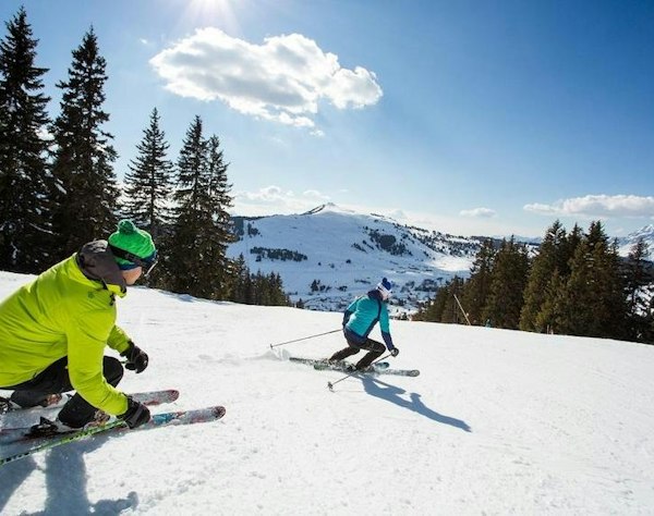 Forfait ski Les Saisies pas cher | Passe Montagne Deux skieurs en virage sur une piste des Saisies bordée de sapins en Savoie