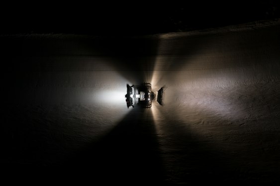 Snow groomer working at night on a ski slope, aerial view, headlights on