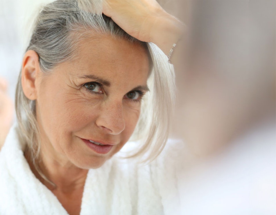 Postmenopause Grauhaarige Frau vor dem Spiegel