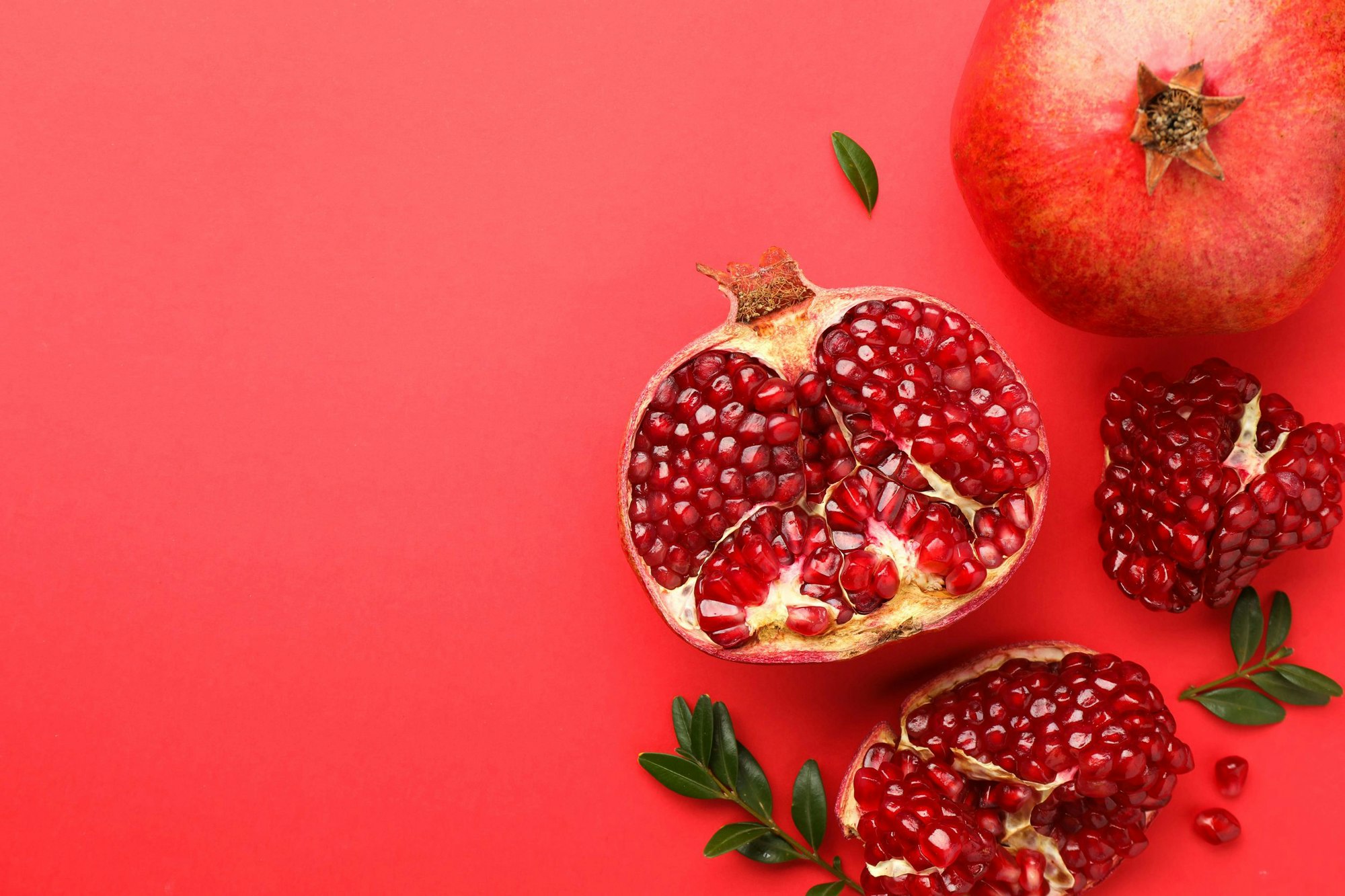 Aufgeschnittener Granatapfel (Punica granatum) mit roten Kernen auf rotem Hintergrund.