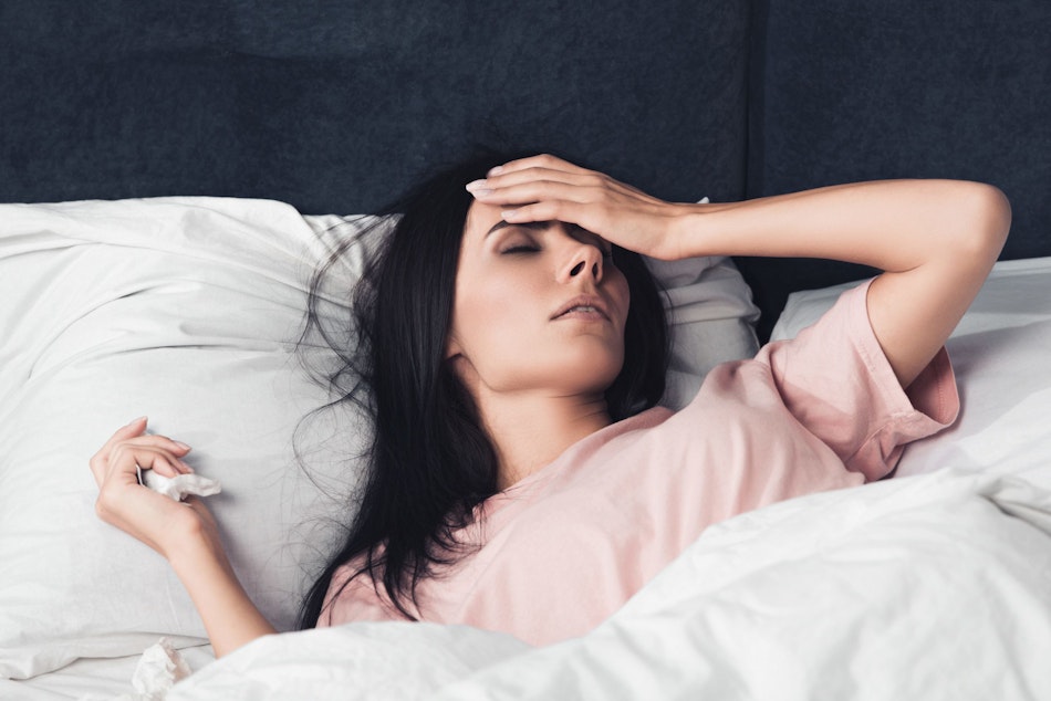Erkältete Frau hält sich die Stirn im Bett