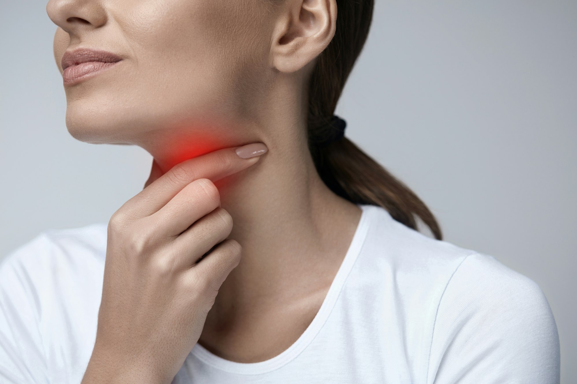 Halsschmerzen beim Schlucken (Foto: AdobeStock, 134619858) Nahaufnahme einer Person, die den Hals berührt. Eine rote Hervorhebung im Halsbereich symbolisiert Halsschmerzen oder eine Reizung des Rachens.