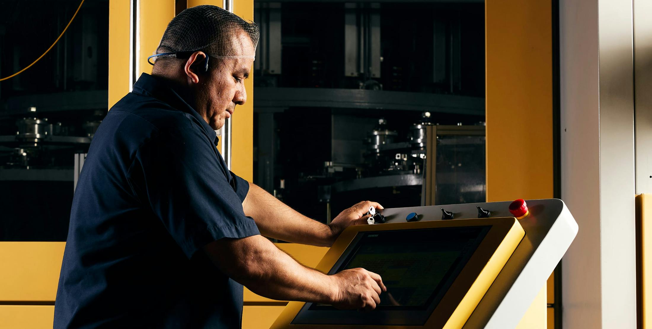 Employee in dark blue collar shirt operating machinery screen in facility