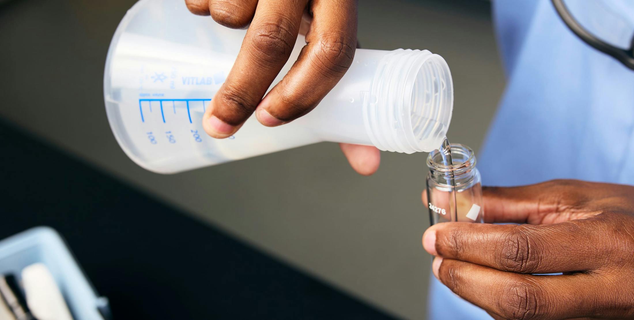 Person pouring measured liquid from a beaker into a test tube