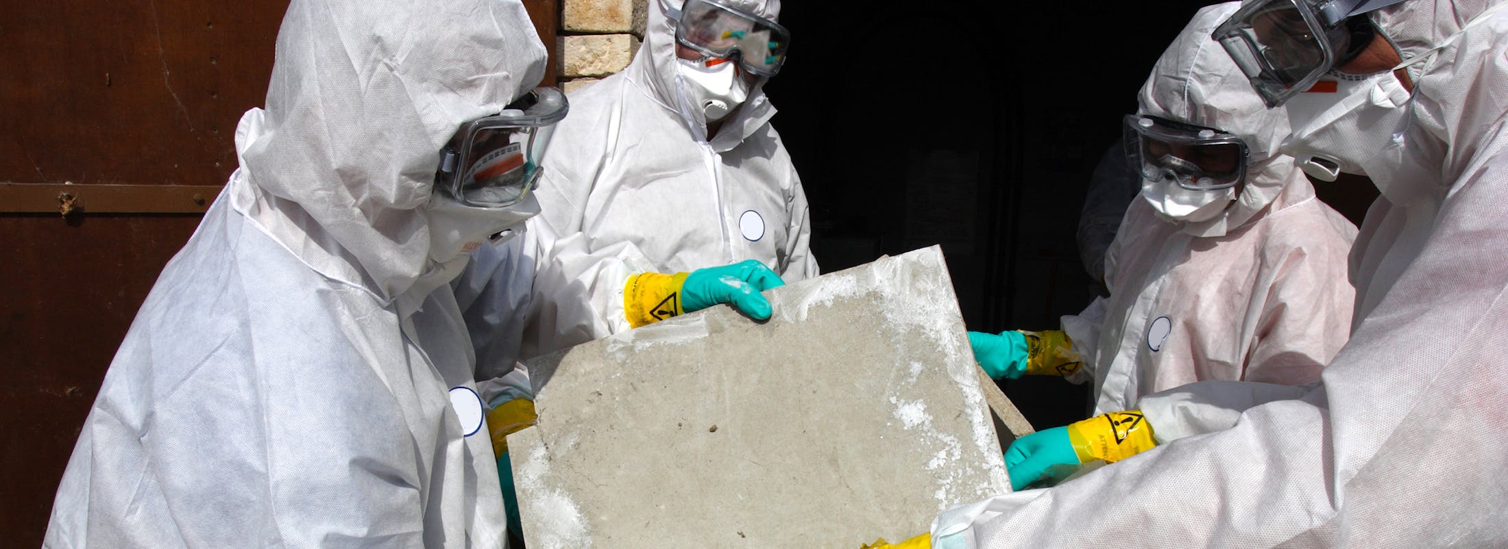 People in hazard suits holding a piece of a building