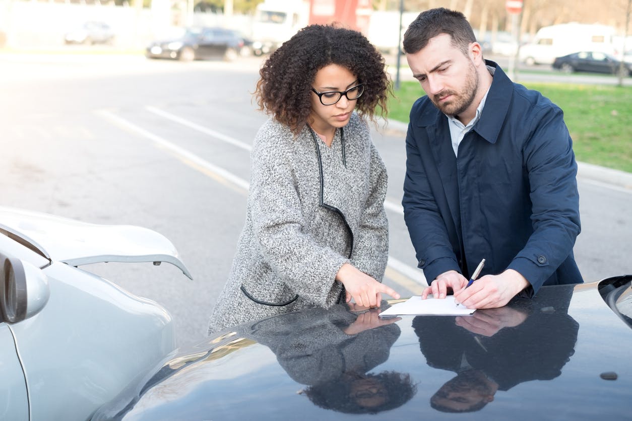 Two people exchanging information next to car accident.