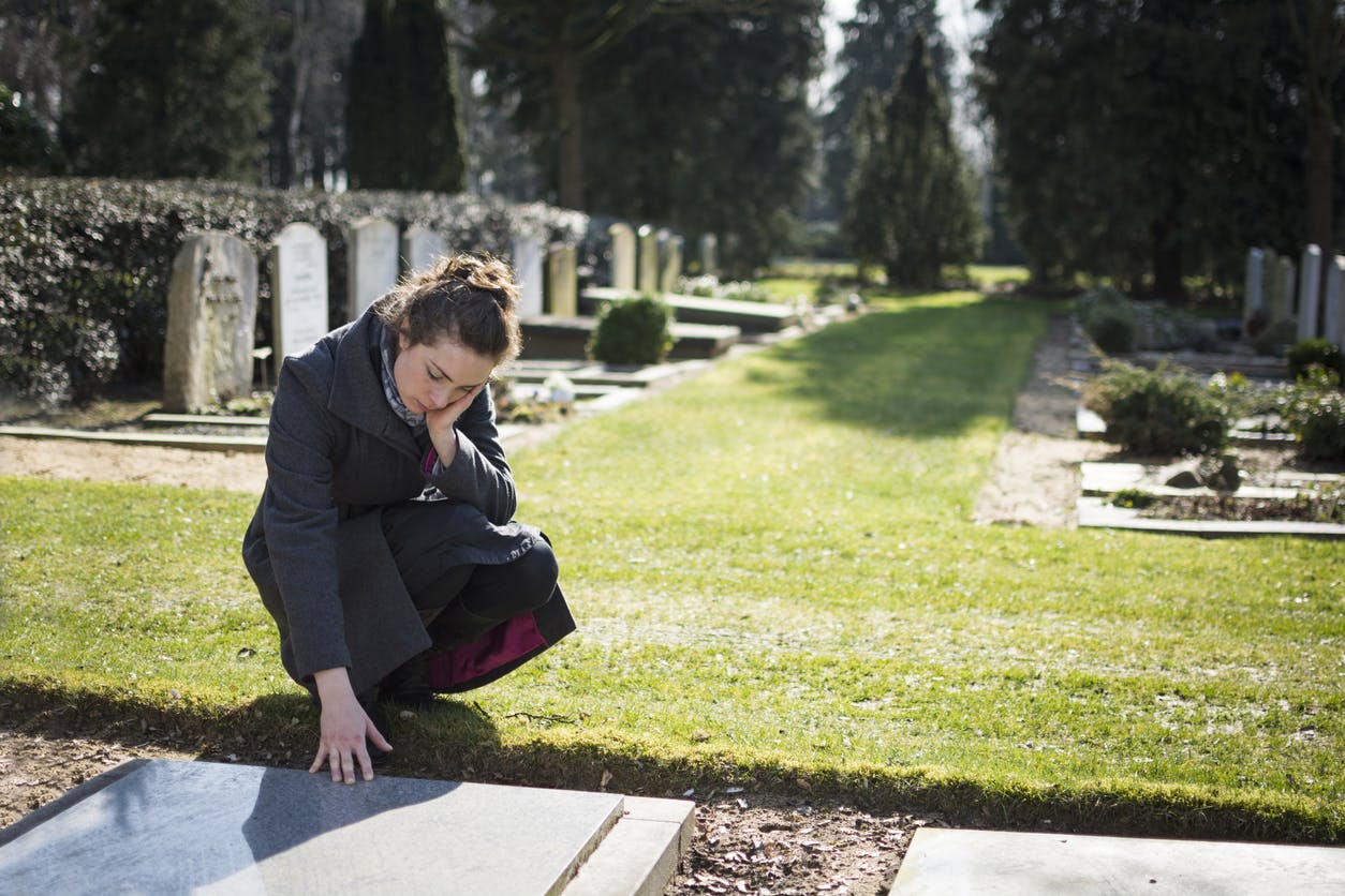 Woman in graveyard with her hand on grave.