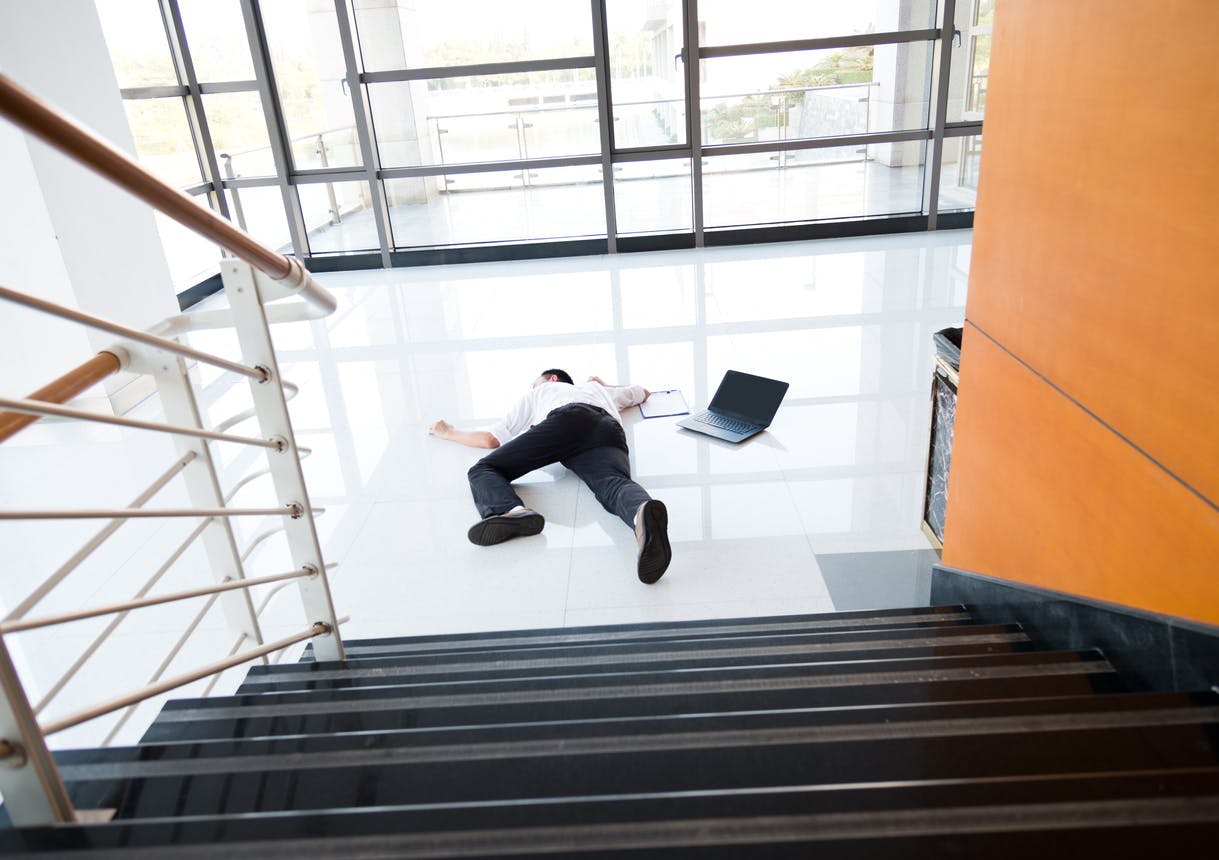 Man fallen on floor at bottom of stairs next to laptop.