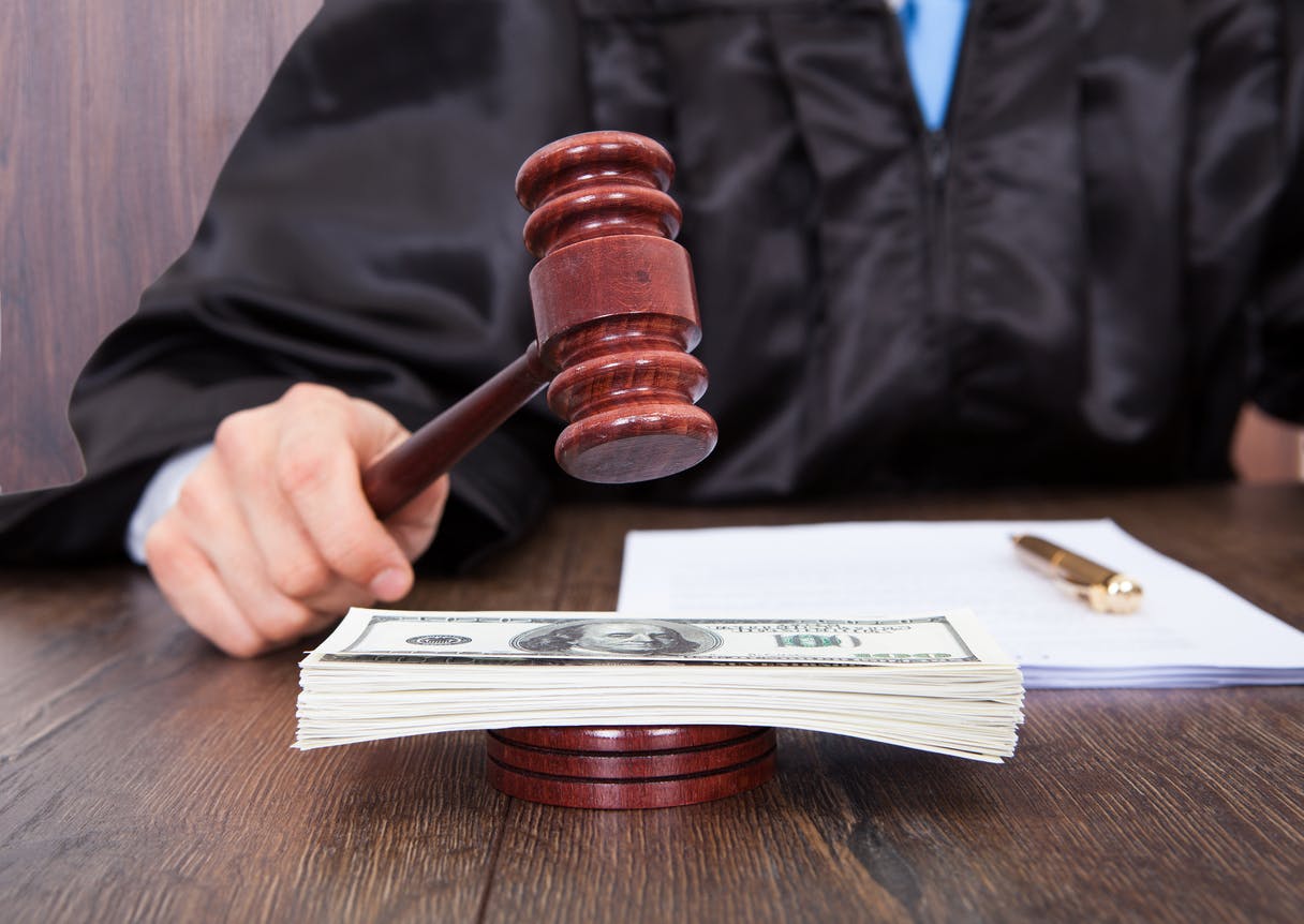 Judge with gavel over stack of money.