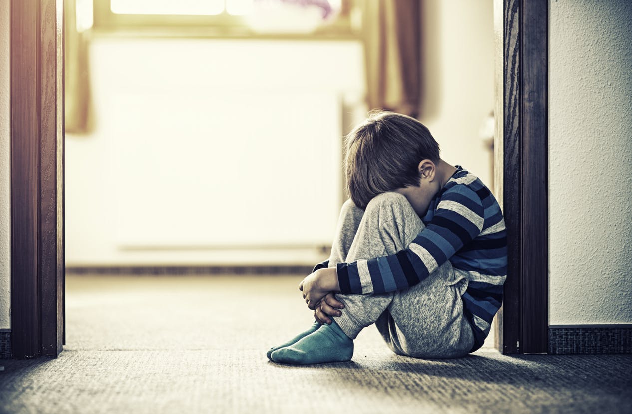 Child sitting against wall, upset