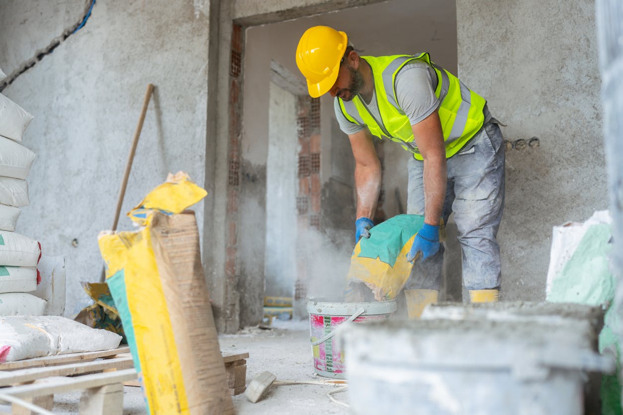 Construction worker mixing grout without a respirator.