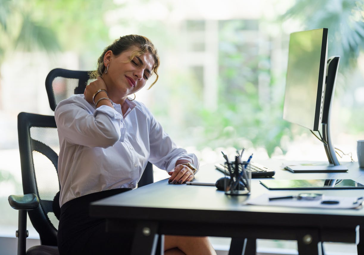 Woman grabbing her neck while sitting at a desk