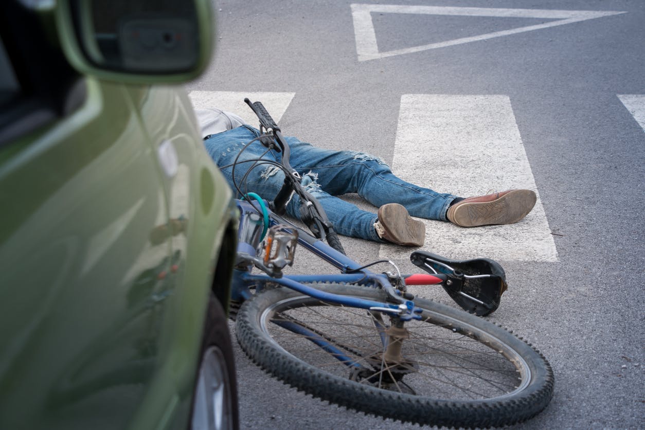 Man lying in a crosswalk next to his bicycle and a car