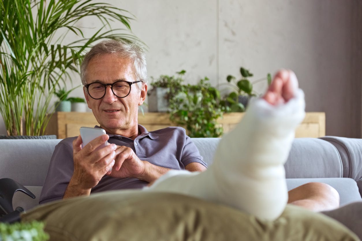 Man with a cast on his foot looking at his phone while sitting on the couch