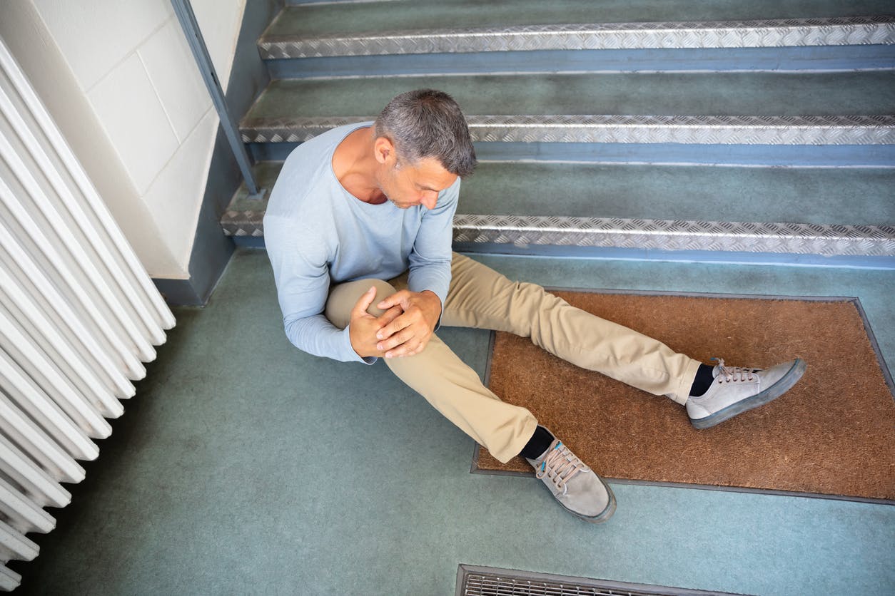 man grabbing his knee while sitting at the bottom of stairs
