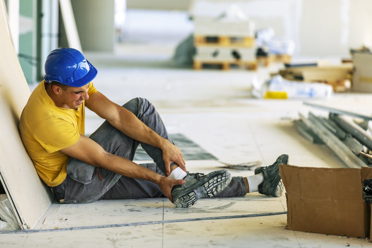 Man grabbing his ankle in pain at a construction site