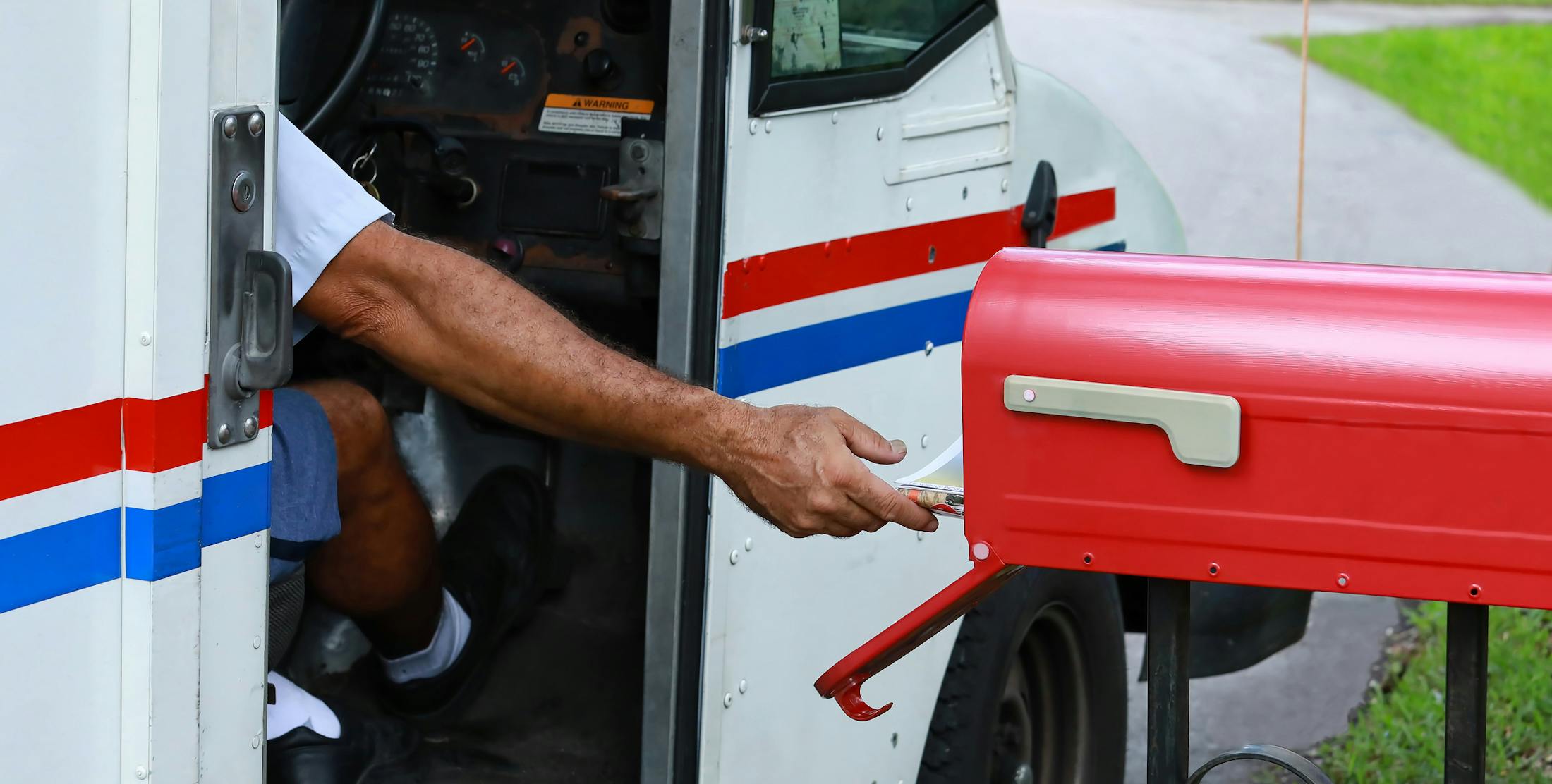 mailman delivering mail into a red mailbox