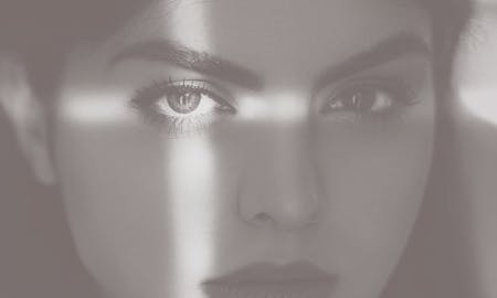 A beautiful woman's shadowed face with light making a cross on her left eye