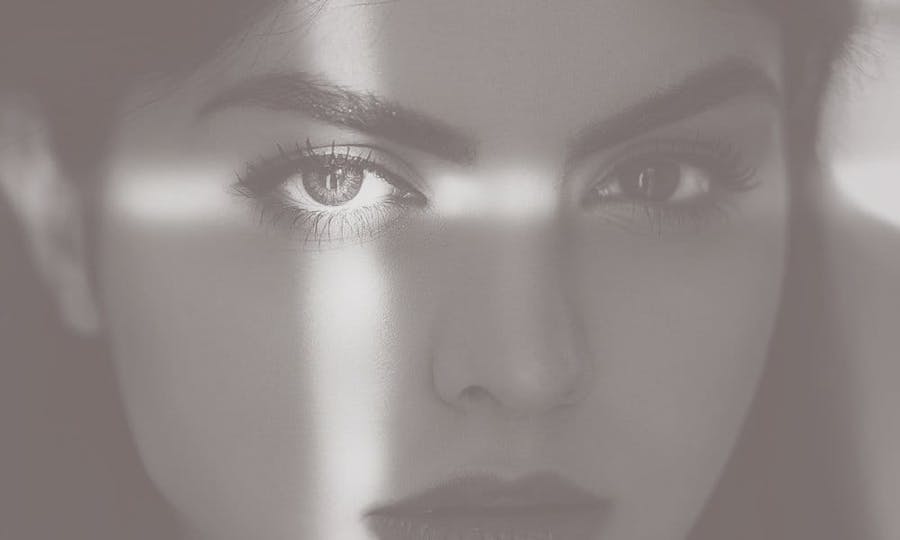 A beautiful woman's shadowed face with light making a cross on her left eye