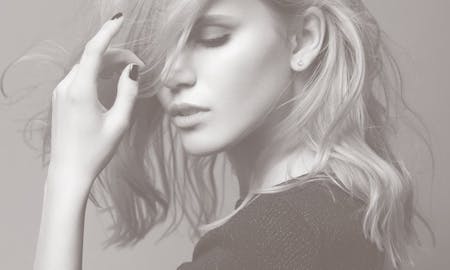 A woman looking down, about to brush her hair back.