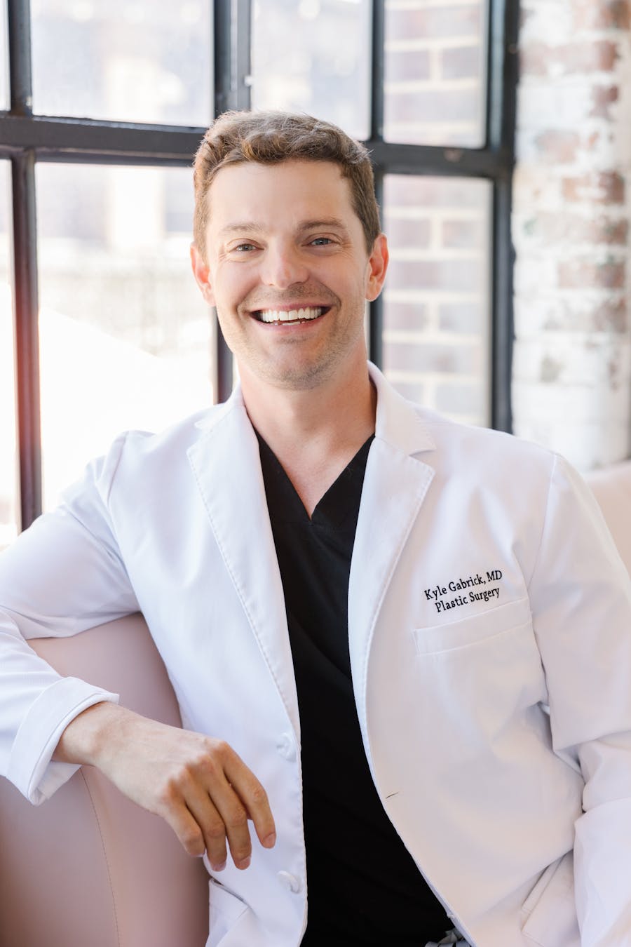 Happy Dr. Gabrick's waering a white doctor's coat leaning against the window sill