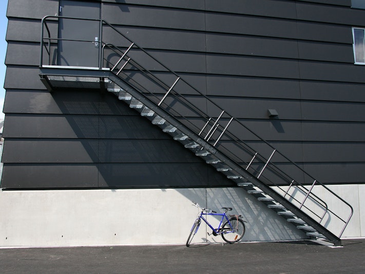 Eine schwarze, gerade Treppe an der Fassade eines Hauses und ein Fahrrad darunter