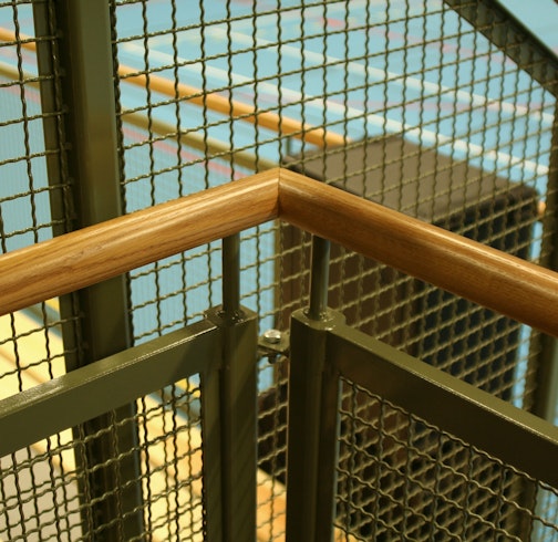Detail picture with wooden handrail and railing in crenelated mesh