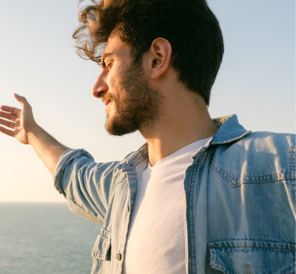man in jean jacket looking to the side with arms raised
