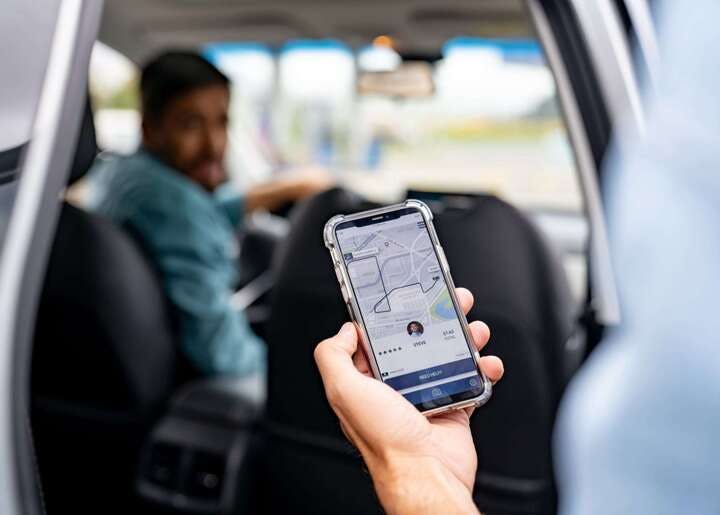 hand holding a phone in a car with uber driver in background