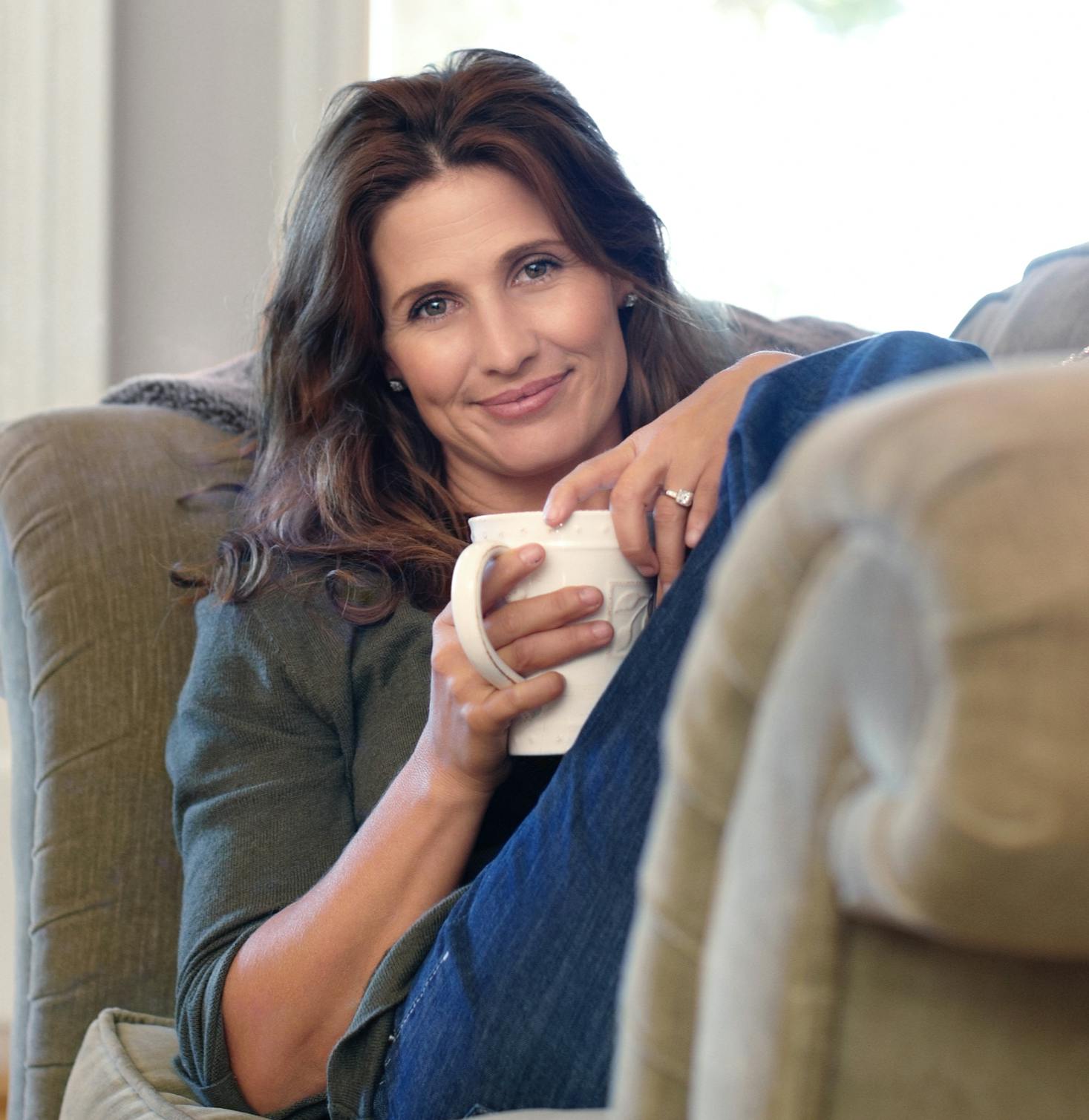 Lady smiling and sitting on a couch drinking coffee