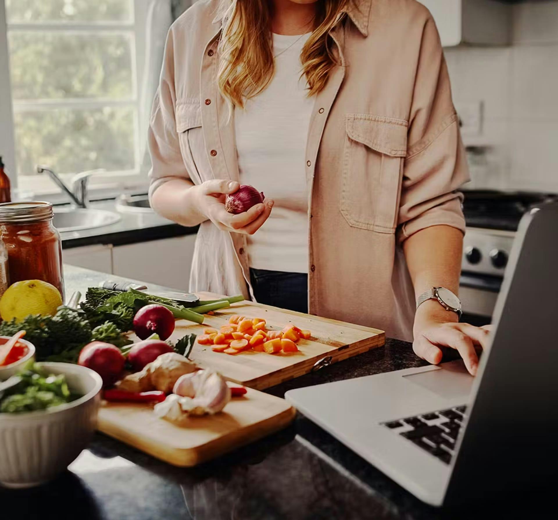 Woman preparing food while looking at a laptop