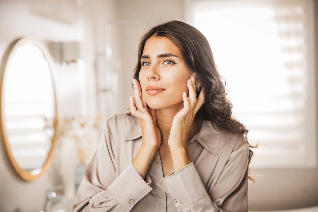 Woman with brown hair feeling her cheeks