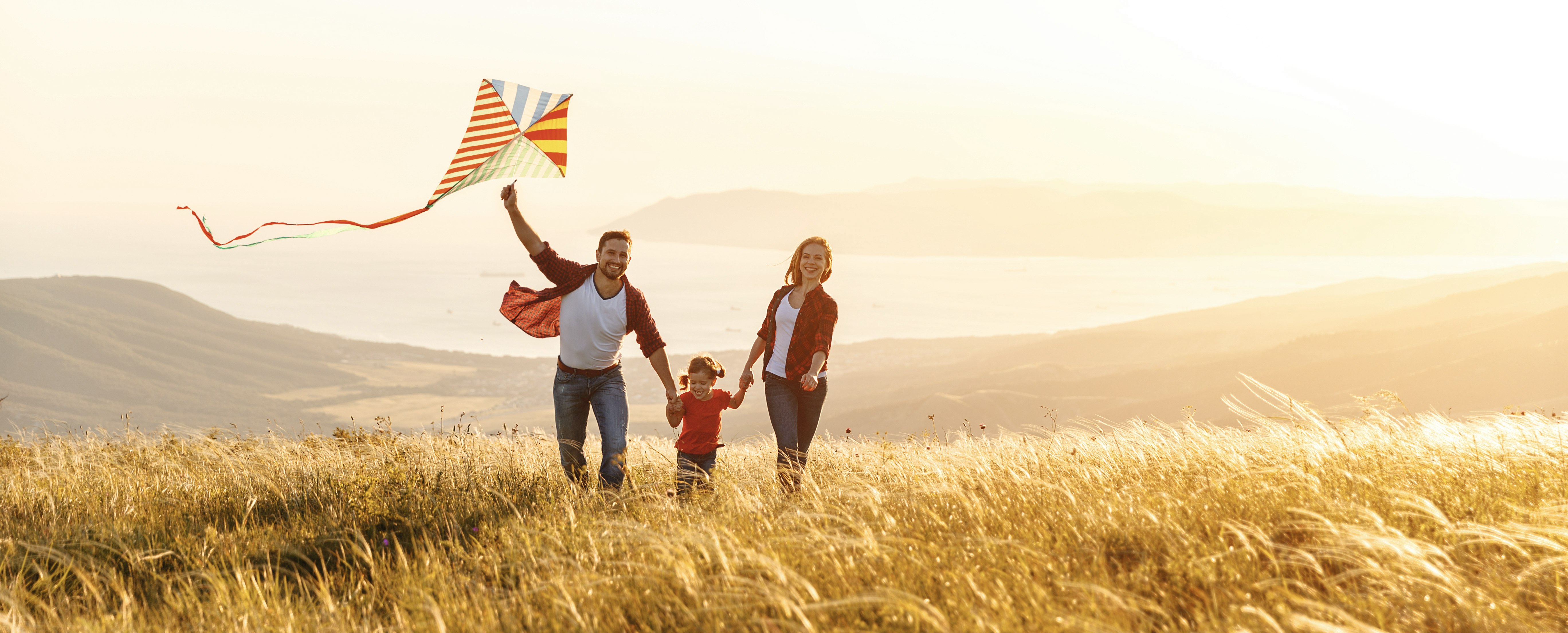 Glänzende Aussichten mit Golden Gates Eine glückliche Familie rennt Hand in Hand über ein golden schimmerndes Kornfeld. Der Vater hält einen Drachen in der Hand. Das Tal im Hintergrund erstrahlt in einem goldenen Licht. Mach auch Sie sich eine Freude und schenken Sie sich oder Ihren Liebsten Gold mit Golden Gates.