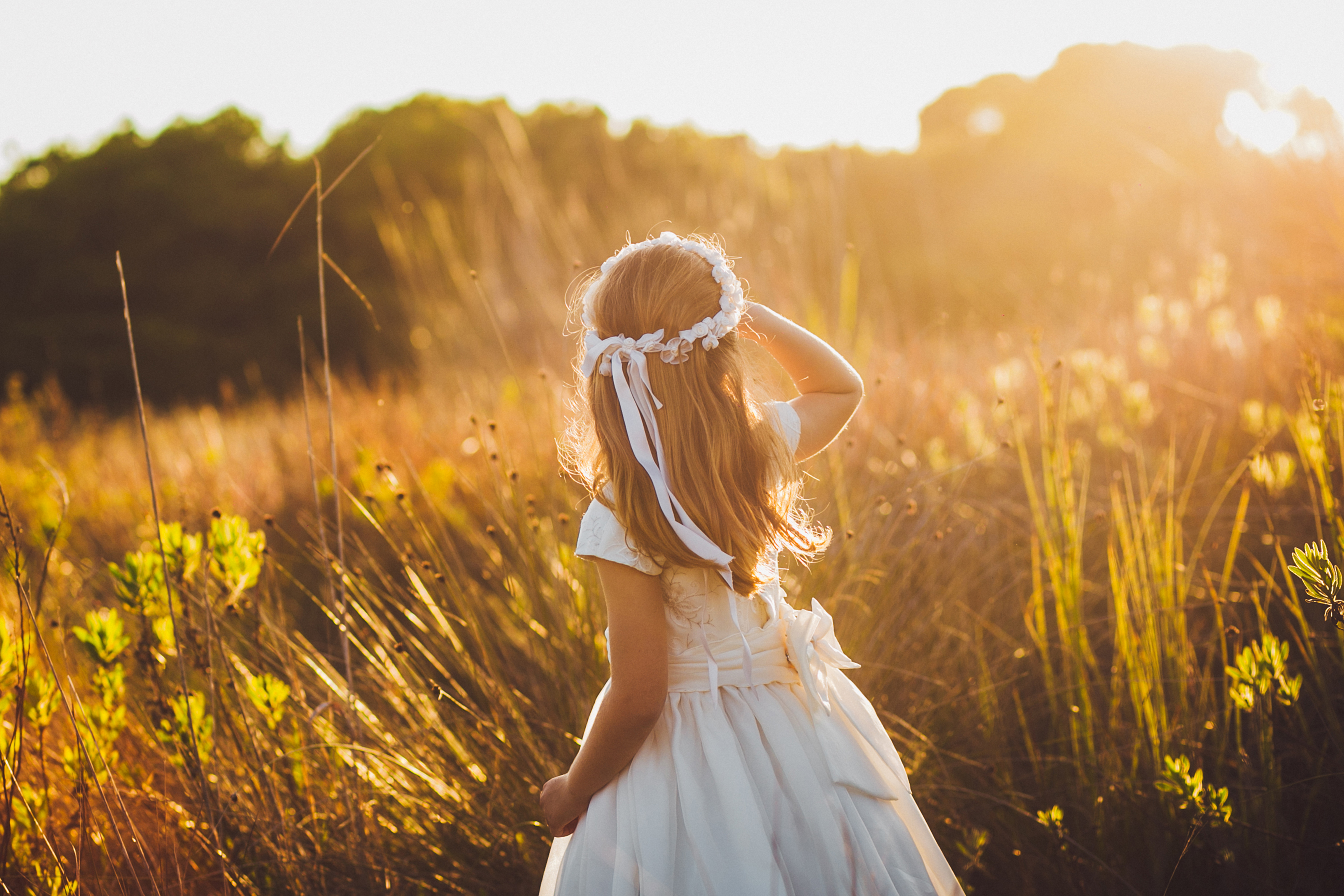 Ein kleines Mädchen, im weißen Kleid, steht in einer Blumenwiese. Es sieht in die Sonne, welche die Wiese in ein strahlendes Gold taucht. Legen auch Sie Geld für Ihre Kinder richtig an und sparen Sie in Anlagemetalle.