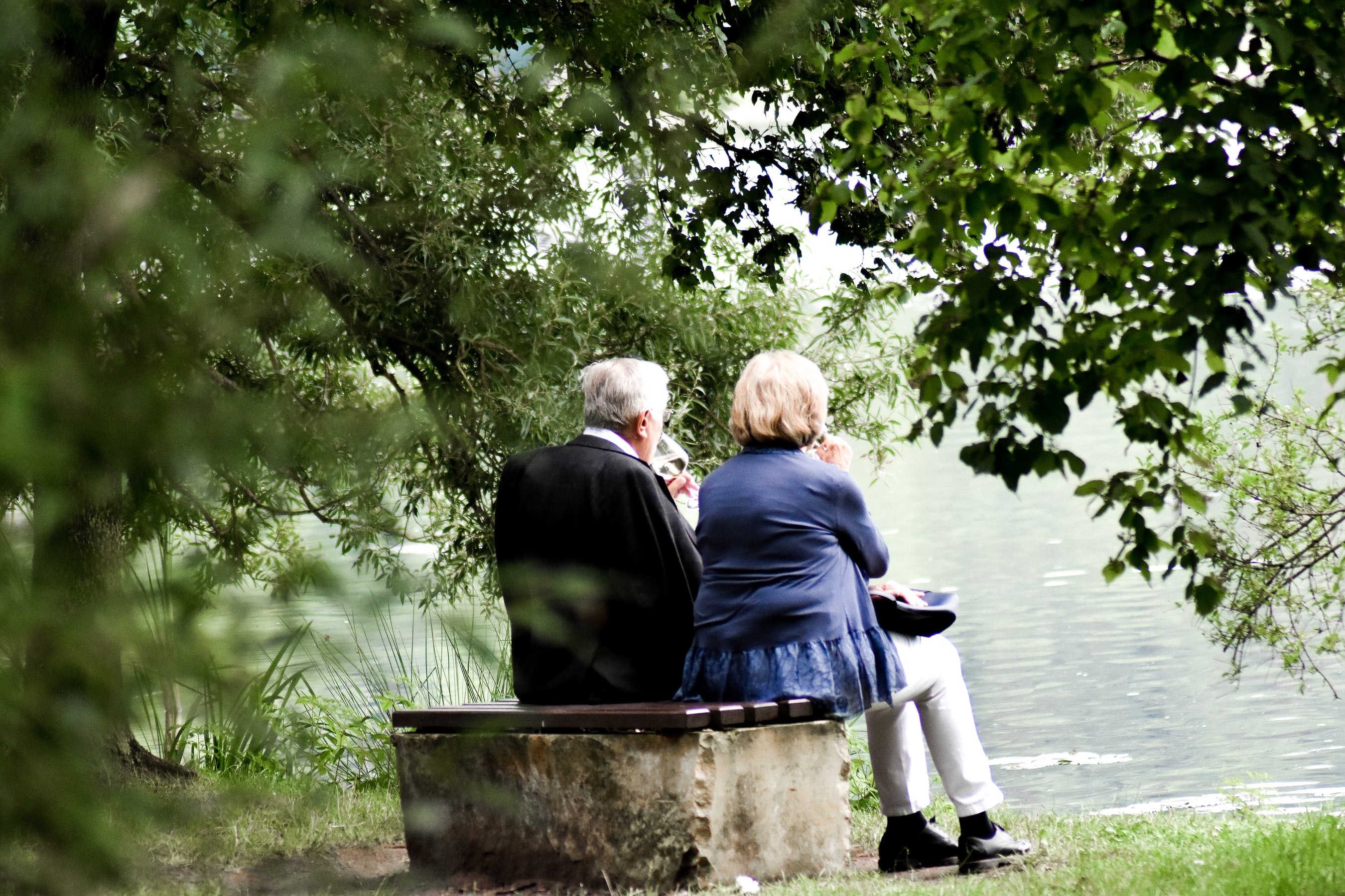 An einem See neben einem Wald, sitzt auf einer Parkbank ein Paar im Rentenalter und schauen auf den See. Altersvorsorge mit Gold und Silber können auch Sie, mit den Sparplänen von Golden Gates.