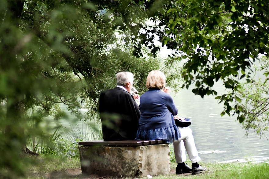 An einem See neben einem Wald, sitzt auf einer Parkbank ein Paar im Rentenalter und schauen auf den See. Altersvorsorge mit Gold und Silber können auch Sie, mit den Sparplänen von Golden Gates.