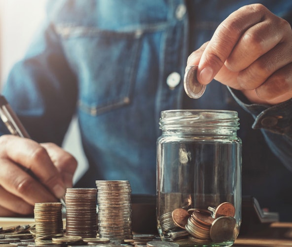 Welche Sparformen sind 2022 noch sinnvoll? In einem hellen Raum sieht man, an einem Tisch eine Person sitzen. Diese zählt Münzen und schreibt die bestände auf. Sparen Sie Ihr Geld mit der Chance auf Wertsteigerung, mit den Edelmetallsparplänen von Golden Gates.