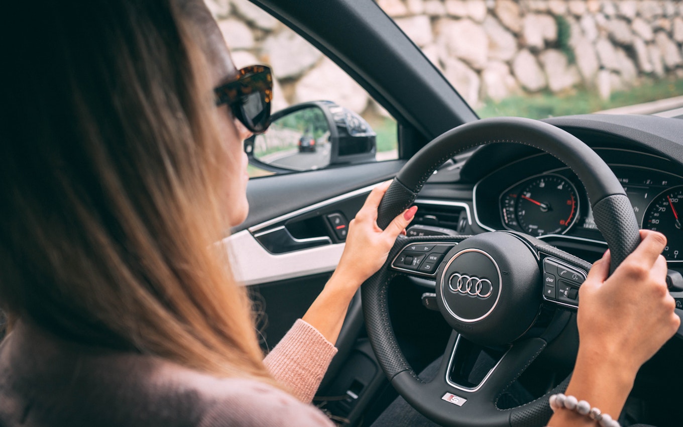 Führerschein Eine junge Person hinter einem Lenkrad auf der Landstraße. Sparen auch Sie für Ihre Zukunft und investieren Sie in Anlagemetalle. Einfach und Flexibel mit den Sparplänen von Golden Gates.