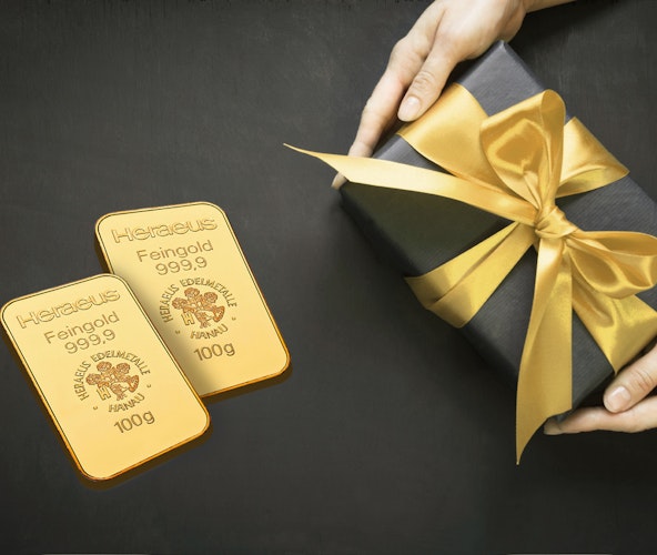 Gold schenken | Golden Gates Auf einem schwarzen Untergrund liegt ein schwarz eingepacktes Geschenk mit goldener Schleife und daneben zwei Goldbarren. Gold für jeden Anlass: Hochzeit, Taufe, Schulanfang, Weihnachten, Geburtstag, mit Golden Gates.