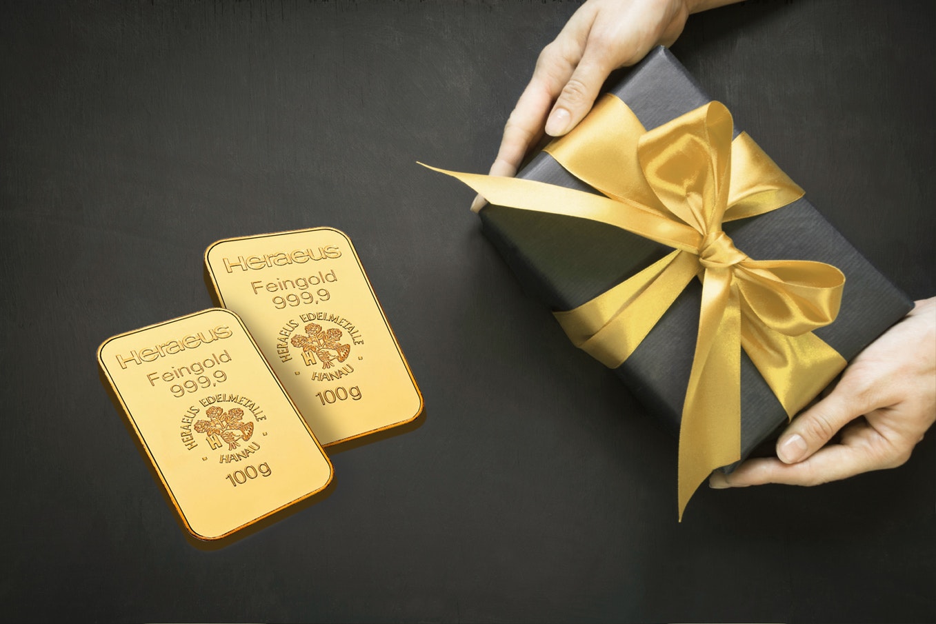 Gold schenken | Golden Gates Auf einem schwarzen Untergrund liegt ein schwarz eingepacktes Geschenk mit goldener Schleife und daneben zwei Goldbarren. Gold für jeden Anlass: Hochzeit, Taufe, Schulanfang, Weihnachten, Geburtstag, mit Golden Gates.
