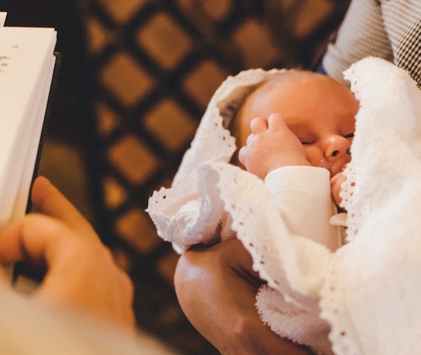 Golden Gates I Geschenke zur Taufe Das Foto wurde über die Schulter des Priesters gemacht, deshalb sieht man einen Teil der Bibel und davor ein Baby in den Armen seiner Mutter. Besondere Momente bedürfen besonderen Geschenken. Mit Golden Gates Gold schenken.