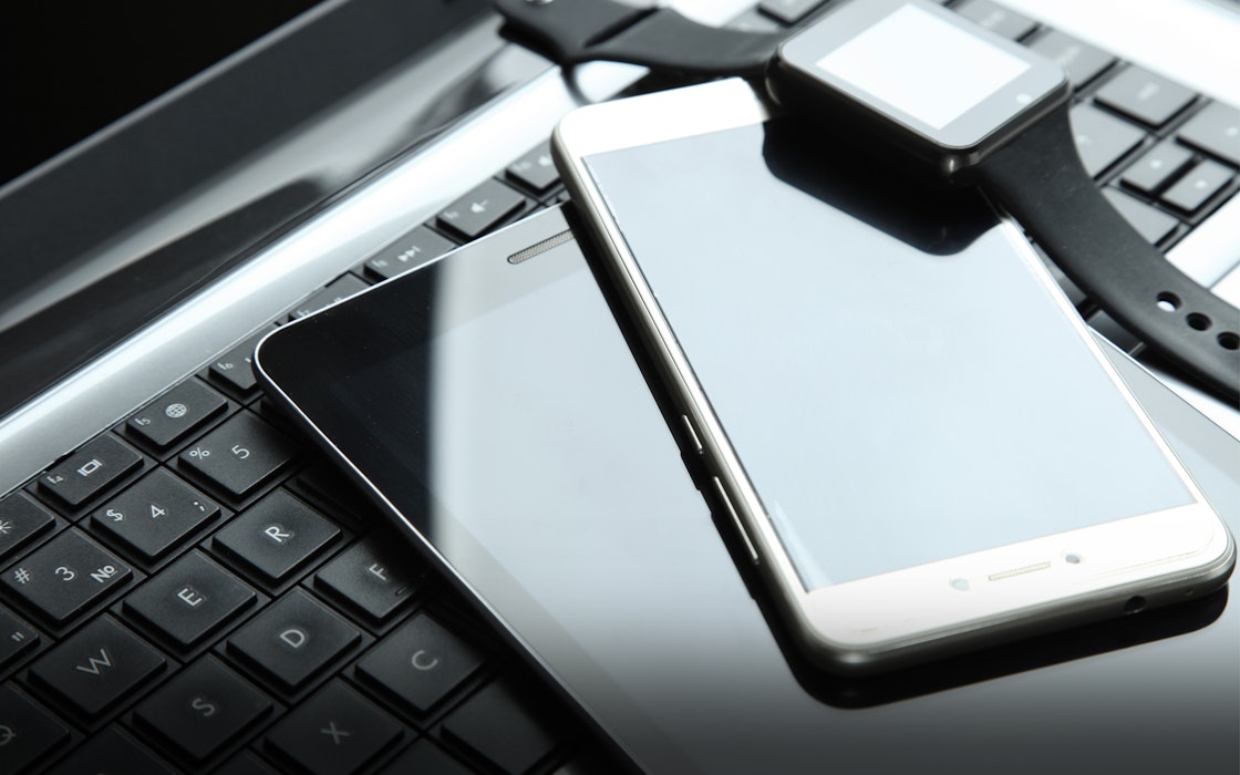 Auf einer Tastatur liegen ein Tablet, ein Handy und eine Smartwatch. Legen auch Sie Ihr Geld richtig an und sparen Sie in Selten Erden mit Golden Gates.
