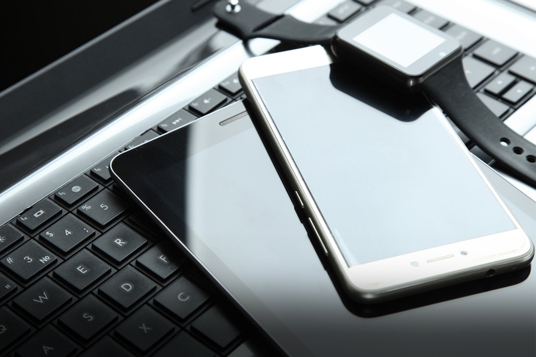 Auf einer Tastatur liegen ein Tablet, ein Handy und eine Smartwatch. Legen auch Sie Ihr Geld richtig an und sparen Sie in Selten Erden mit Golden Gates.