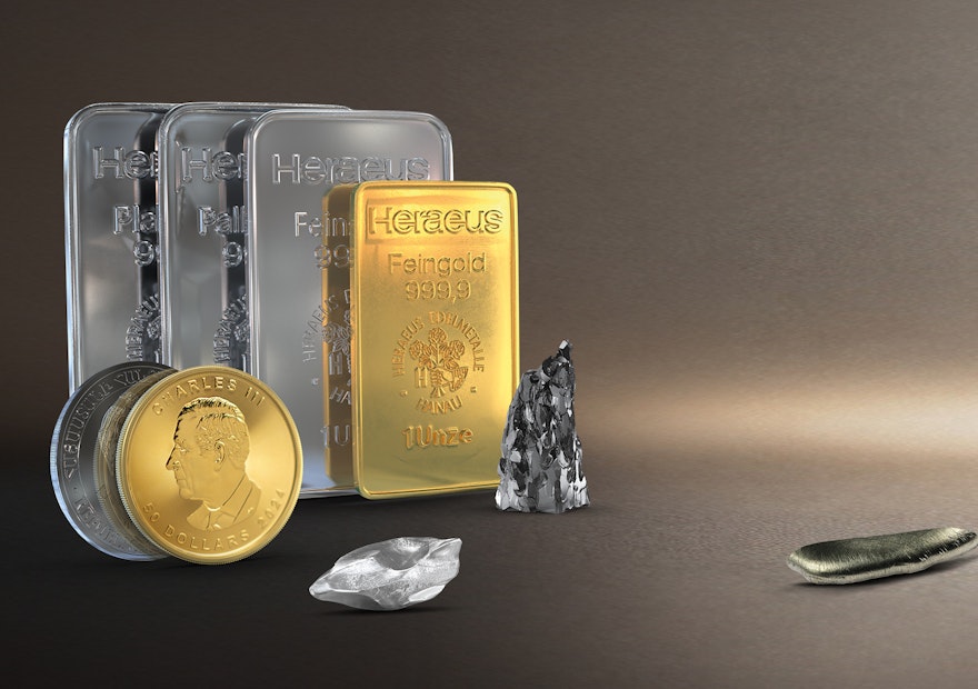Vor einem erdfarbenen Hintergrund sind Edelmetallbarren, eine Gold- und Silbermünze Technologiemetalle und Seltene Erden abgebildet. Sparen auch Sie in Anlagemetalle mit den Sparplänen von Golden Gates.
