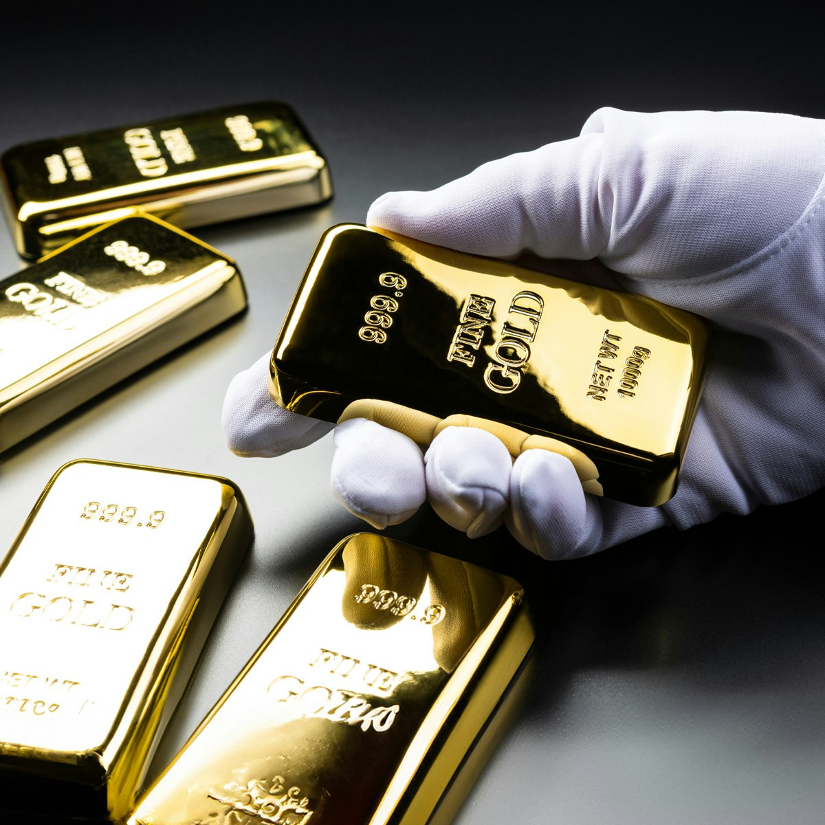 Goldbarren die auf einem Tisch liegen und eine Hand im weißen Handschuh hält einen von diesen. Gold ist eine optimale Anlageoption. Jetzt sparen mit den Sparplänen von Golden Gates.