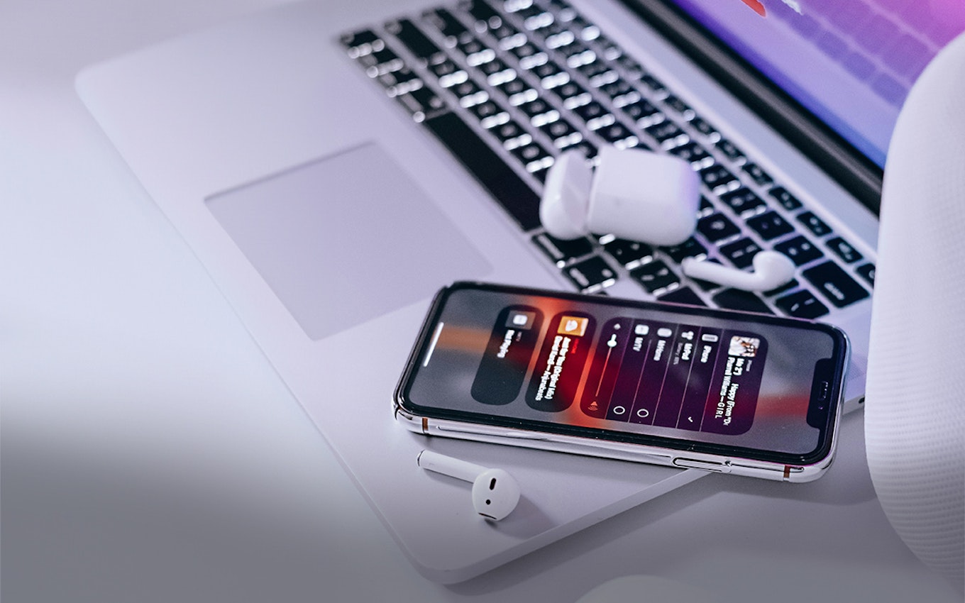 Elektronik Auf einem weißen Tisch liegt ein offener Laptop. Auf dem Rand des Laptops liegen ein Handy und In-Ear-Kopfhörer. In Anlagemetalle sparen mit den Sparplänen von Golden Gates.