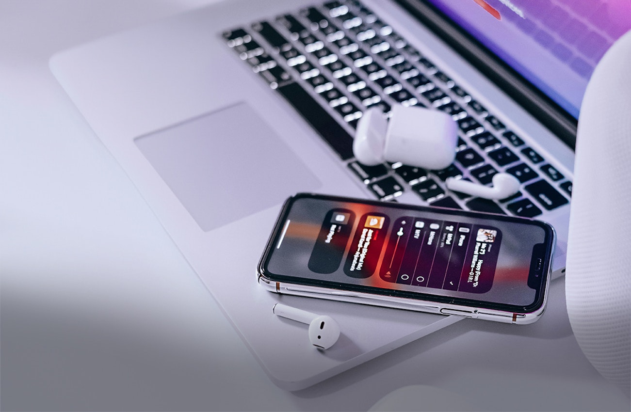 Auf einem weißen Tisch liegt ein offener Laptop. Auf dem Rand des Laptops liegen ein Handy und In-Ear-Kopfhörer. In Anlagemetalle sparen mit den Sparplänen von Golden Gates.
