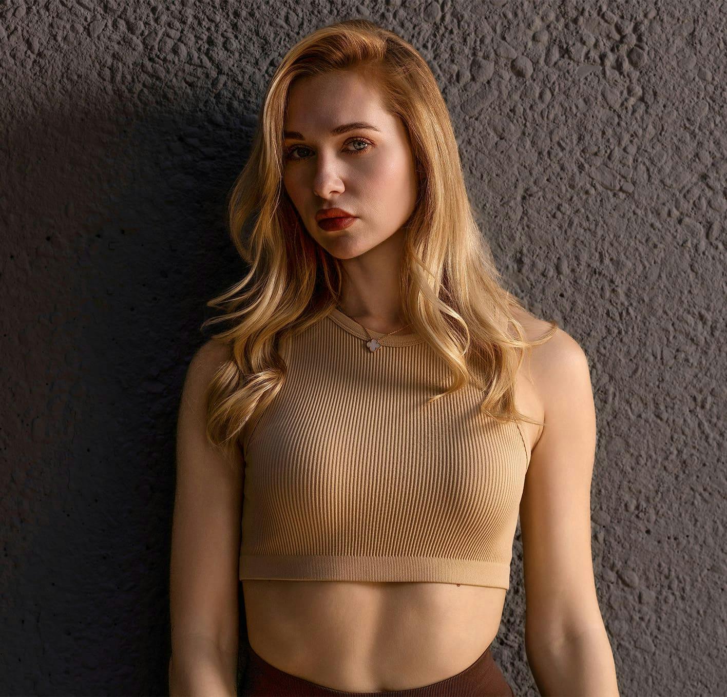 woman standing in front of gray wall in beige top